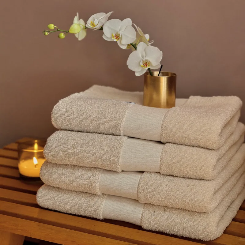 Stack of folded cream spa towels with a candle and a white orchid