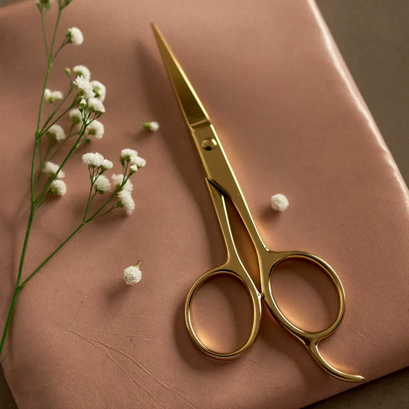 Polished gold hair scissors on a blush leather pouch with tiny white flowers