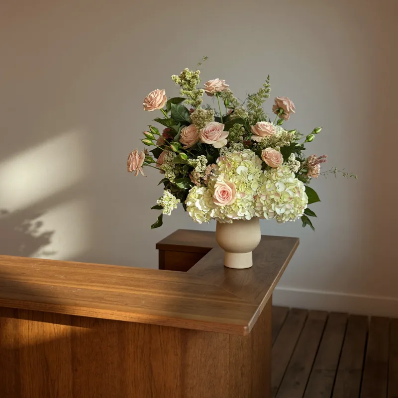 Front desk corner with a lush arrangement of blush roses and cream hydrangeas