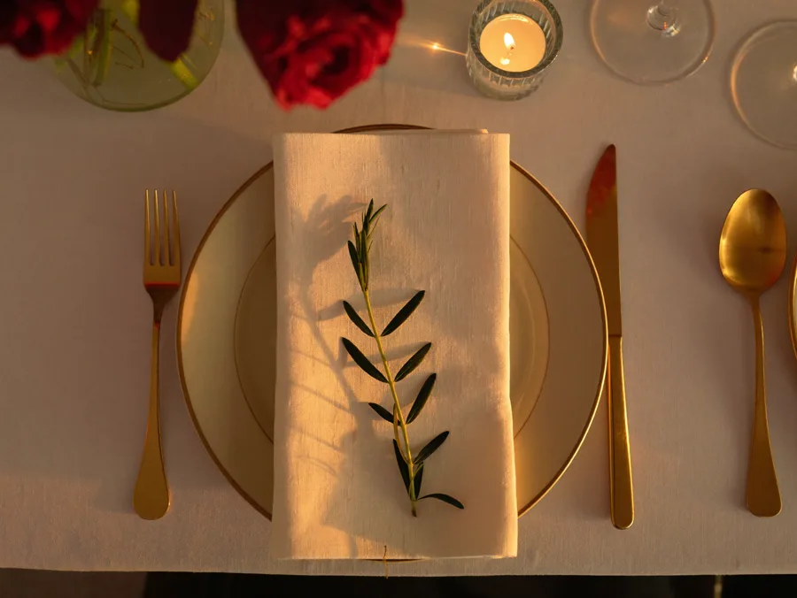 Gold-rimmed place setting with a folded cream napkin and olive sprig, seen from above
