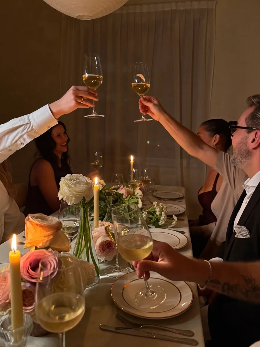 Friends raising champagne glasses in a toast over a candlelit private dinner table