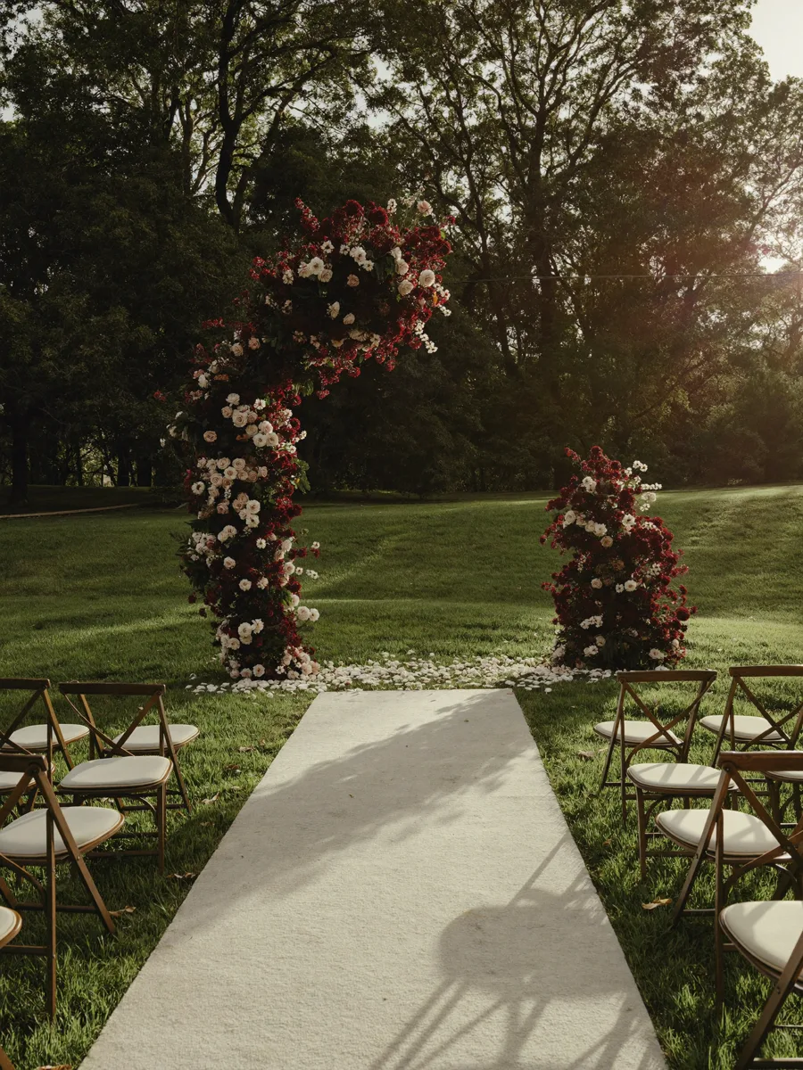 Floral ceremony arch at golden hour with a petal-lined aisle and rows of chairs